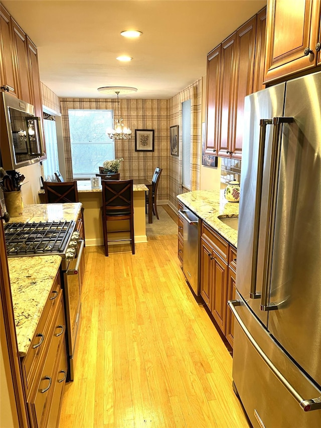 kitchen with premium appliances, decorative light fixtures, light wood-style floors, and light stone counters