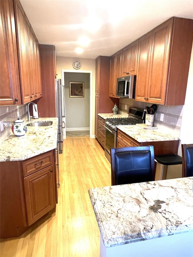 kitchen featuring appliances with stainless steel finishes, backsplash, a sink, and light wood-style flooring