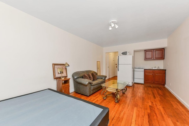 bedroom with light wood finished floors, a sink, freestanding refrigerator, and baseboards