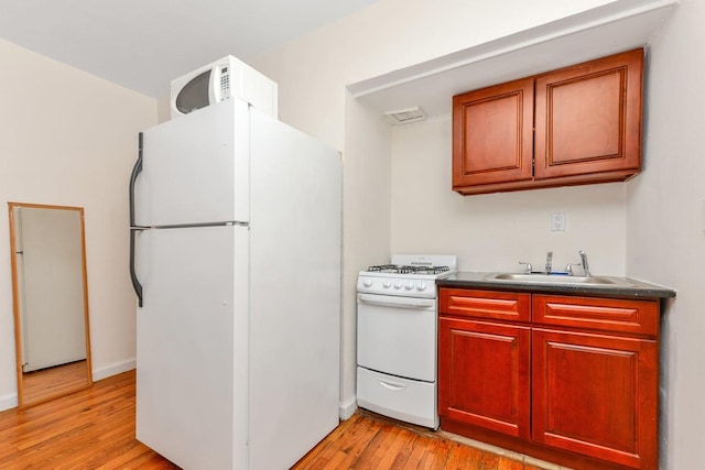 kitchen with white appliances, dark countertops, a sink, and light wood-style floors