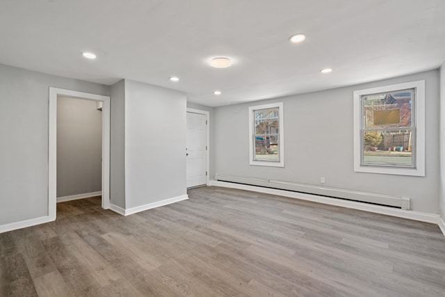 spare room featuring a baseboard heating unit, baseboards, wood finished floors, and recessed lighting