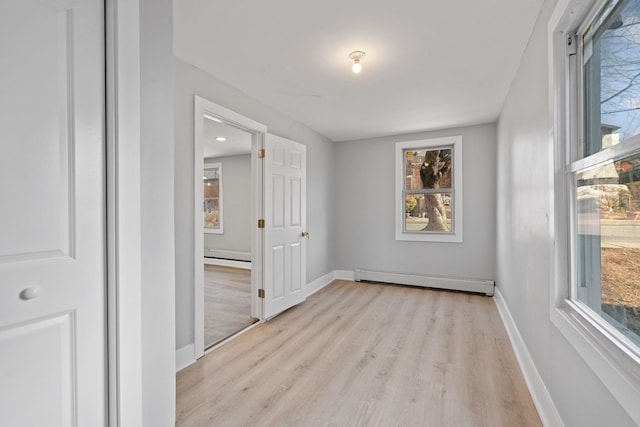 empty room featuring light wood-style floors, a baseboard radiator, and baseboards