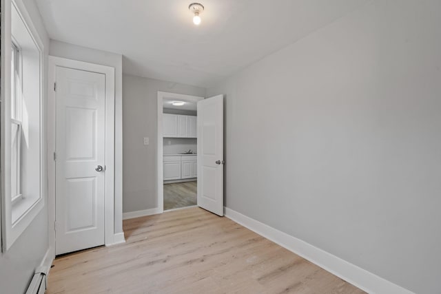 unfurnished bedroom with light wood-style floors, a baseboard radiator, and baseboards