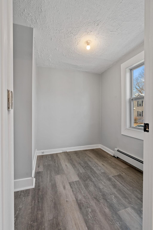 spare room featuring a textured ceiling, baseboard heating, wood finished floors, and baseboards