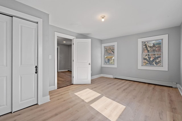 unfurnished bedroom with a baseboard heating unit, light wood-type flooring, and baseboards