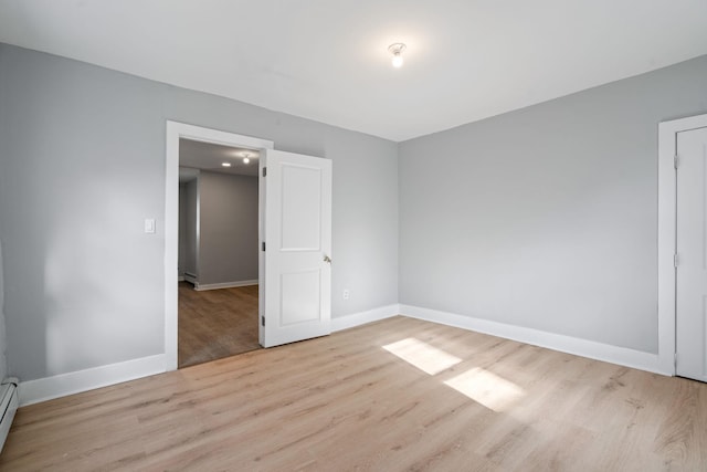 unfurnished bedroom featuring a baseboard heating unit, a baseboard radiator, baseboards, and wood finished floors