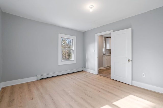 unfurnished room with a baseboard radiator, baseboards, and light wood-style flooring