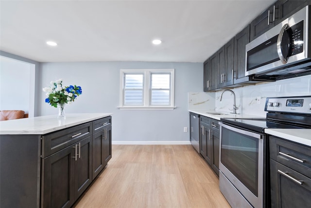 kitchen with light wood finished floors, tasteful backsplash, appliances with stainless steel finishes, a sink, and baseboards