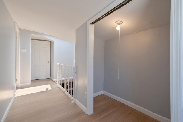 corridor featuring baseboards, an upstairs landing, and wood finished floors