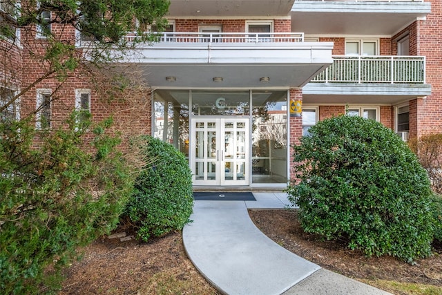 view of exterior entry with a balcony, french doors, and brick siding