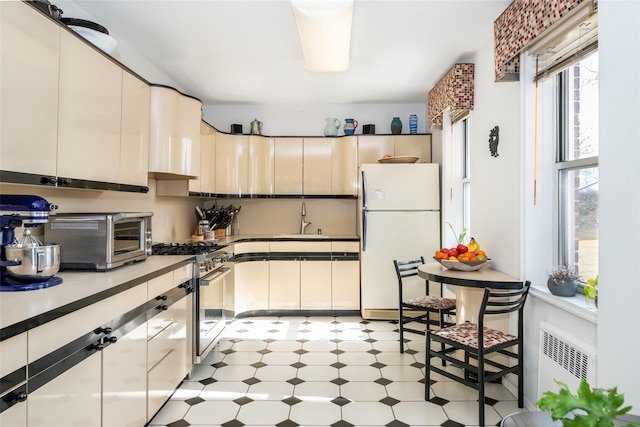 kitchen with a toaster, radiator heating unit, freestanding refrigerator, gas stove, and a sink