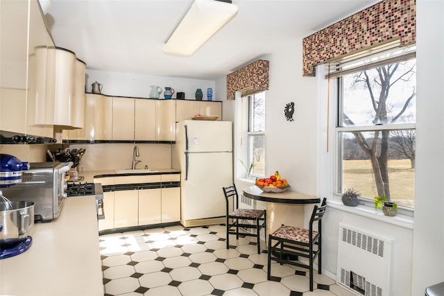 kitchen with a sink, radiator, light floors, and freestanding refrigerator