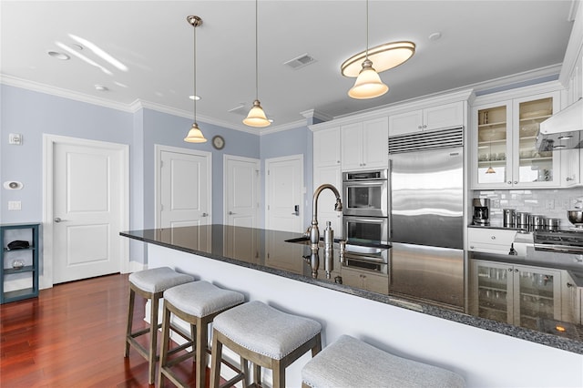 kitchen with backsplash, ornamental molding, appliances with stainless steel finishes, dark wood-style floors, and white cabinetry