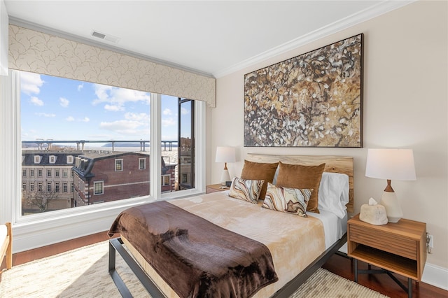 bedroom featuring wood finished floors, visible vents, baseboards, and ornamental molding