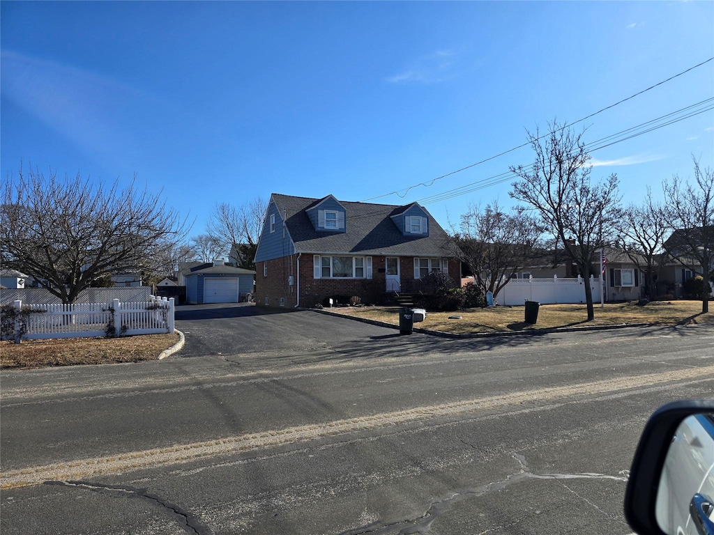 cape cod-style house with brick siding, an outdoor structure, fence, driveway, and a residential view