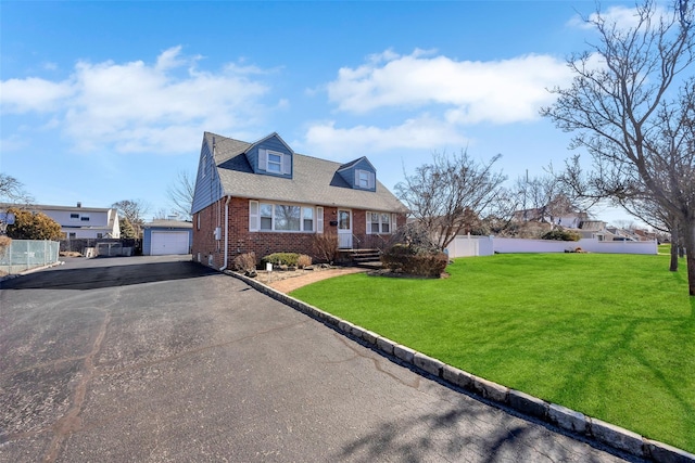 view of front of property featuring an outbuilding, a front lawn, aphalt driveway, fence, and brick siding