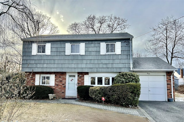 view of front facade featuring a garage, driveway, brick siding, and roof with shingles