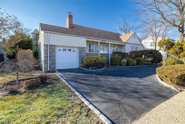 ranch-style home with an attached garage, a shingled roof, driveway, stone siding, and a chimney