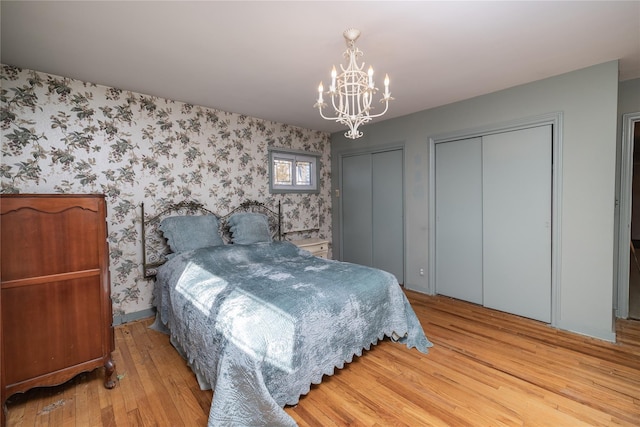 bedroom featuring a chandelier, multiple closets, wood finished floors, and wallpapered walls