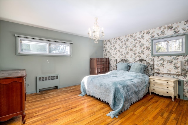 bedroom with radiator heating unit, an inviting chandelier, wood finished floors, and wallpapered walls