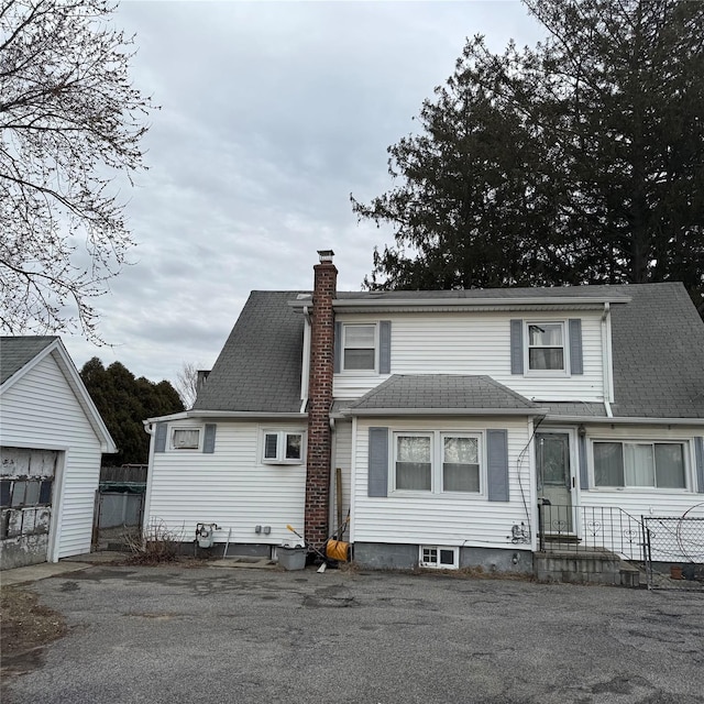 view of front facade featuring a chimney, an outbuilding, and roof with shingles