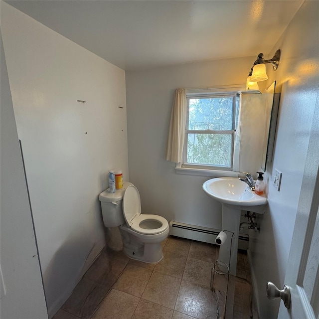 half bath featuring tile patterned flooring, toilet, a baseboard heating unit, a sink, and baseboards