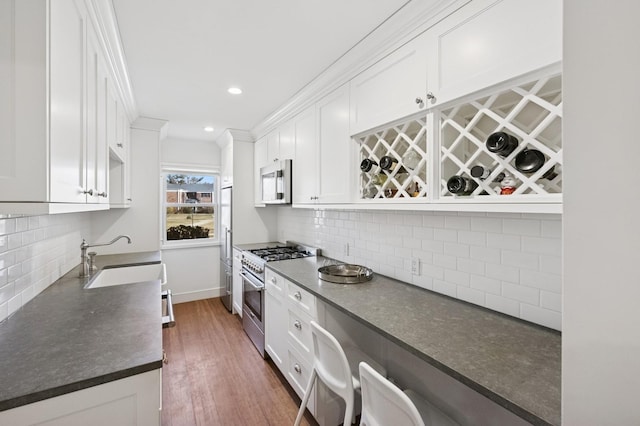 kitchen with tasteful backsplash, high end appliances, dark countertops, white cabinetry, and a sink