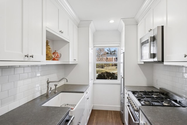 kitchen with stainless steel appliances, dark countertops, a sink, and white cabinetry