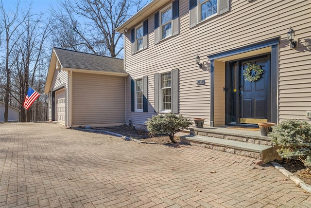 doorway to property with a garage, decorative driveway, and a shingled roof