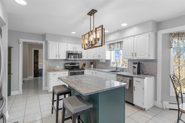 kitchen with a sink, backsplash, white cabinets, stainless steel appliances, and a baseboard radiator