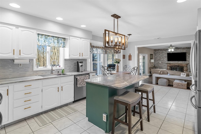 kitchen with open floor plan, light tile patterned floors, a fireplace, stainless steel appliances, and a sink