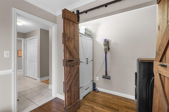 interior space with a barn door, wood finished floors, crown molding, and baseboards