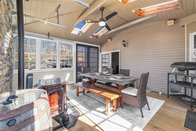 sunroom featuring lofted ceiling with skylight, a ceiling fan, wood ceiling, and a wood stove