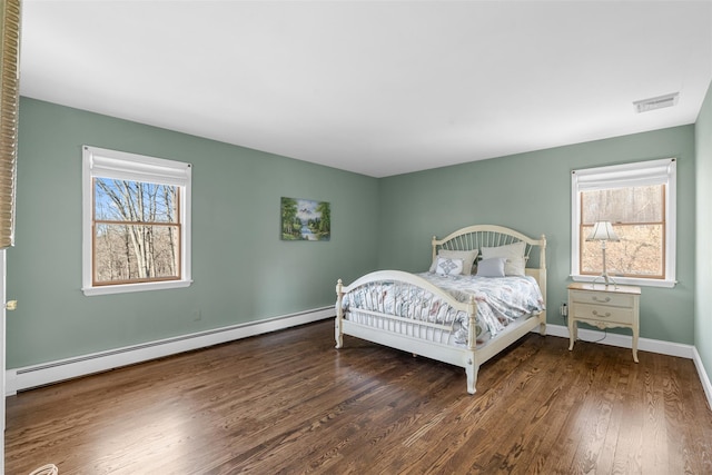 bedroom with a baseboard heating unit, multiple windows, wood finished floors, and baseboards