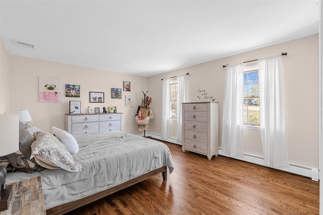 bedroom featuring visible vents, a baseboard heating unit, and wood finished floors