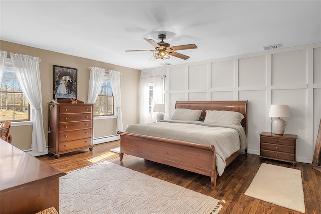 bedroom featuring visible vents, a baseboard heating unit, wood finished floors, a decorative wall, and ceiling fan