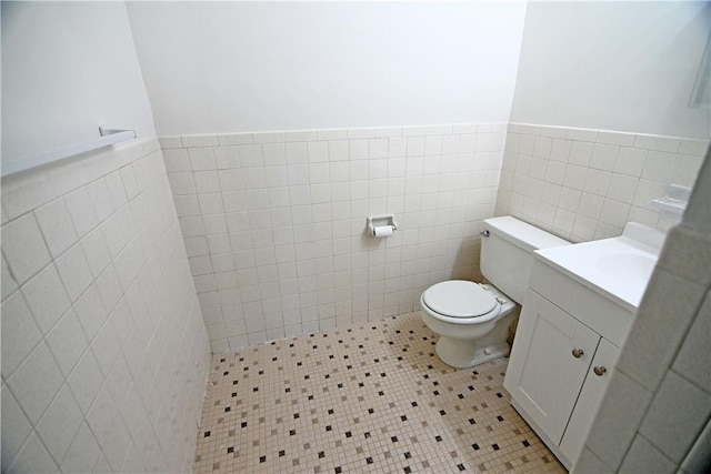 bathroom featuring wainscoting, vanity, toilet, and tile walls