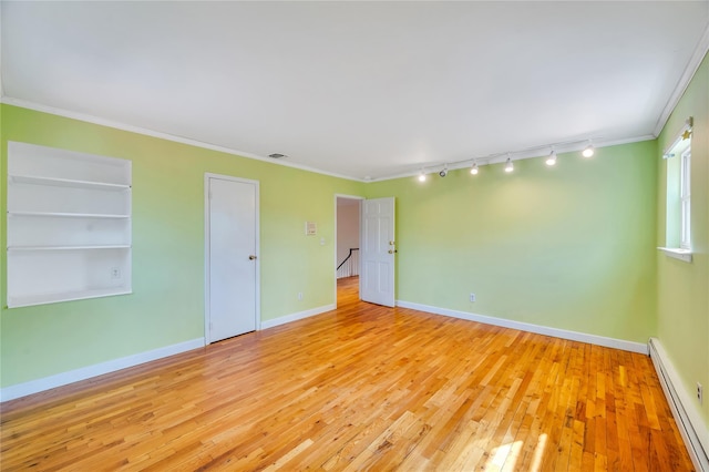 spare room featuring built in shelves, a baseboard radiator, baseboards, ornamental molding, and hardwood / wood-style floors