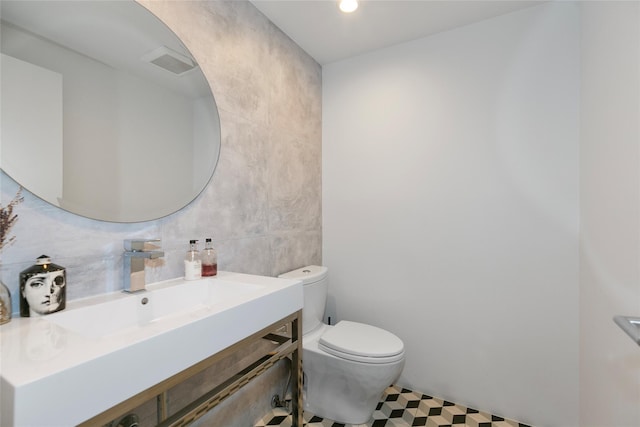 half bathroom featuring visible vents, toilet, tile patterned floors, vanity, and tile walls