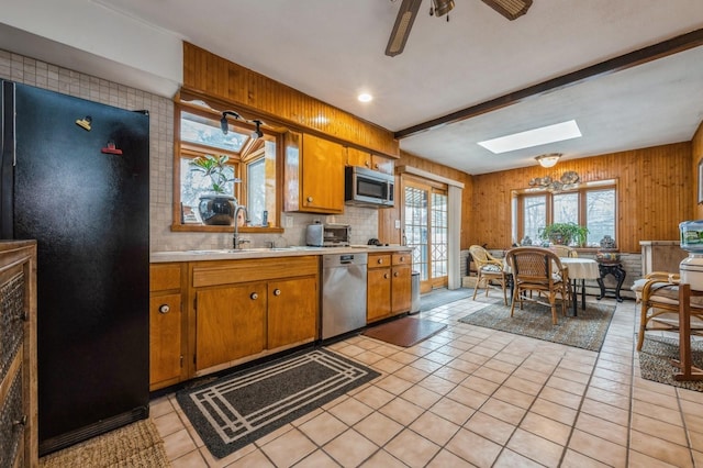 kitchen featuring a skylight, stainless steel appliances, light countertops, brown cabinetry, and a sink