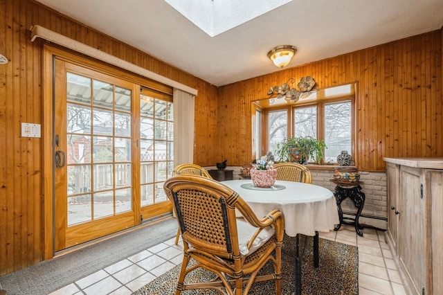 dining area with a baseboard heating unit, a skylight, wood walls, and light tile patterned floors