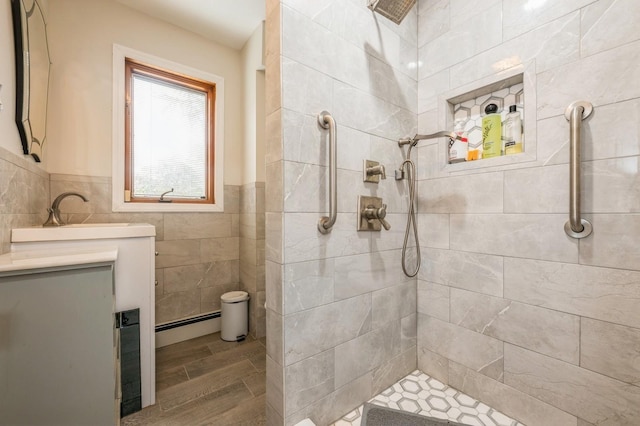 full bathroom featuring tile walls, tiled shower, vanity, and baseboard heating