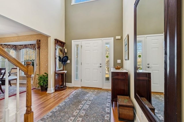 entrance foyer with stairway, wood finished floors, baseboards, ornamental molding, and a towering ceiling