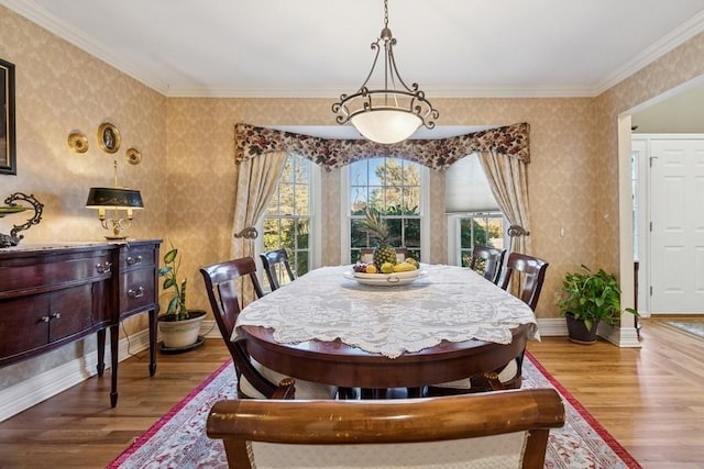 dining area featuring wallpapered walls, crown molding, baseboards, and wood finished floors