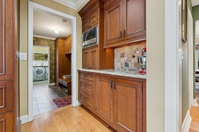 bar featuring ornamental molding, stainless steel microwave, washer / clothes dryer, light wood-style floors, and decorative backsplash