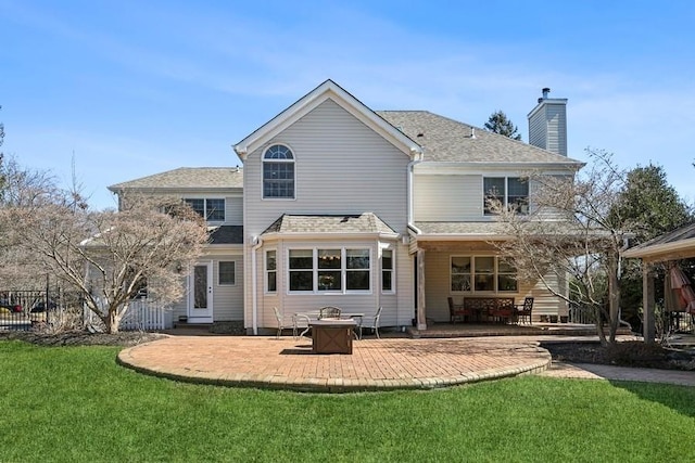 back of house featuring a lawn, fence, roof with shingles, a chimney, and a patio area