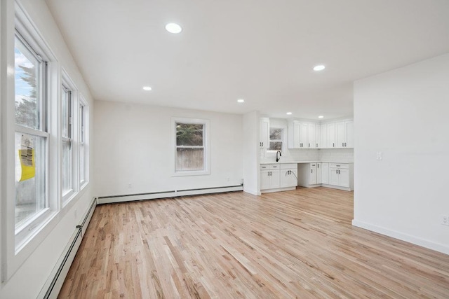 unfurnished living room featuring a wealth of natural light, light wood-type flooring, and baseboard heating