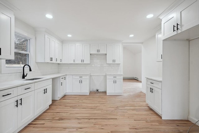 kitchen with white cabinets, light wood-style floors, decorative backsplash, and a sink