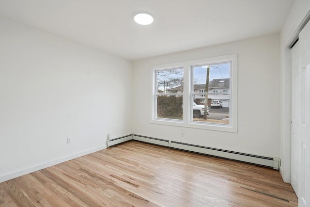 unfurnished bedroom with light wood-type flooring, baseboards, a baseboard heating unit, and a closet