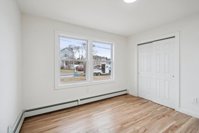 unfurnished bedroom featuring a baseboard radiator, a closet, and light wood finished floors